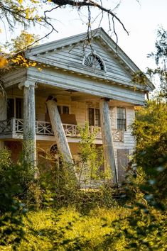 an old run down house in the middle of some bushes and trees with stairs leading up to it