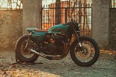 a green motorcycle parked in front of a gated area with autumn leaves on the ground