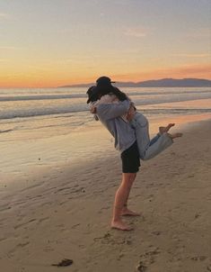 two people are hugging on the beach at sunset