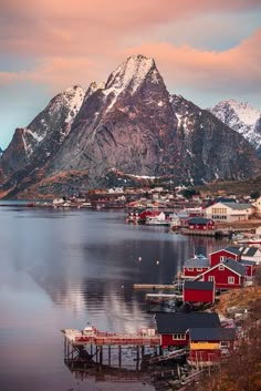 the mountains are covered in snow and red houses sit on the water's edge