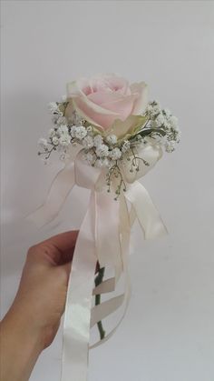 a person is holding a pink rose with white flowers and greenery on the side