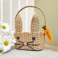 a woven basket with a carrot and bunny ears on it next to some daisies