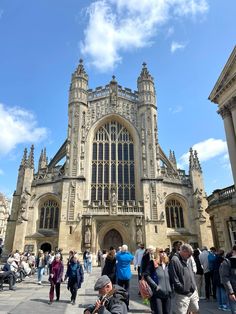 many people are walking around in front of an old building with tall towers and arched windows