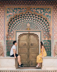 a man and woman are sitting on the steps in front of a wooden door with intricate designs