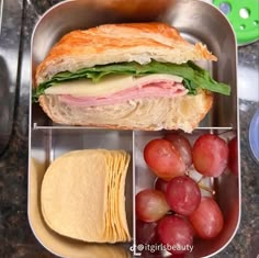 a sandwich in a metal container with grapes and crackers