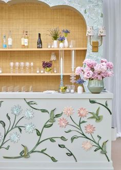 a bar with flowers painted on the front and shelves behind it, along with vases filled with flowers