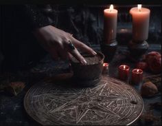 a person with their hand on a bowl in the middle of a table surrounded by candles