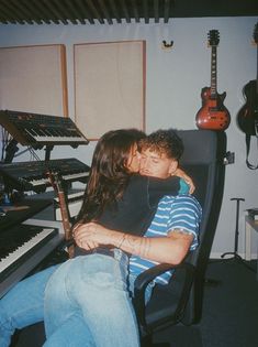 a man and woman sitting in front of a keyboard with guitars on the wall behind them