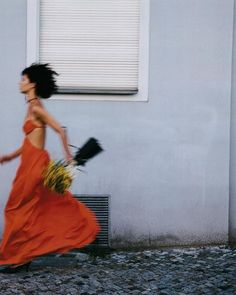 a woman in an orange dress is walking down the street with her hair blowing in the wind