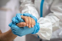 two people in white coats and blue gloves holding each other's hands with one hand