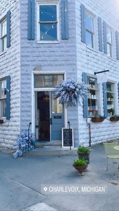 a white brick building with blue shutters on the front and side windows, next to an outdoor table and chairs