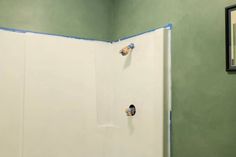 a bathroom with green walls and blue tape on the shower wall, which is being painted white