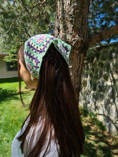 a woman with long hair wearing a crocheted hat in front of a tree