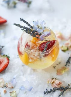 a glass filled with fruit and ice on top of a white table covered in flowers