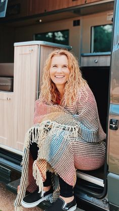 a woman sitting in the back of a truck with a blanket over her shoulders and smiling