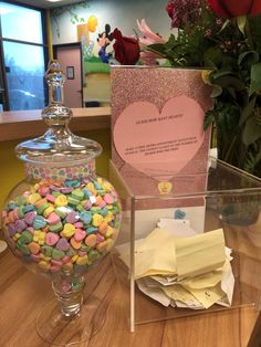 there is a glass vase with candy in it and a card on the table next to it