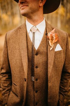 a man wearing a brown suit and flower boutonniere, standing in the woods