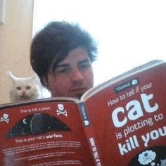 a man reading a book with a cat sitting on top of his head next to him