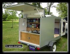 an outdoor kitchen is built into the back of a trailer with its door open and shelves on it