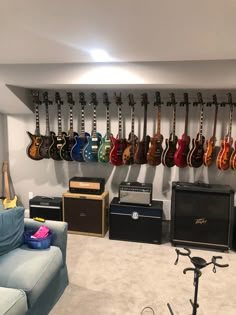 a room with guitars and amps hanging on the wall next to a couch in front of a guitar rack