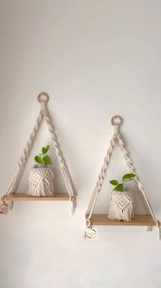 two white vases with green plants on top of them hanging from the side of a wall