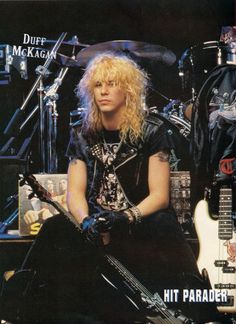 a man with long blonde hair sitting in front of a guitar and posing for the camera