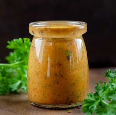 a jar filled with sauce sitting on top of a wooden table next to parsley