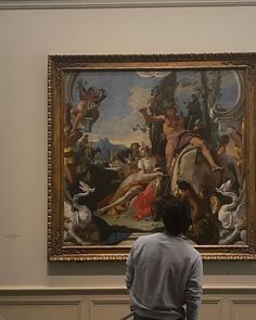 a man sitting on a bench looking at a large painting in a museum with people standing around it