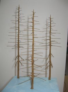 three wooden trees on top of a blue table in front of a white wall with wires attached to it