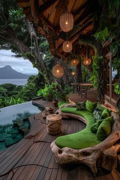 a wooden deck with green cushions and lights hanging from it's ceiling next to a swimming pool