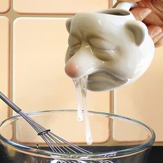 a person pouring milk into a glass bowl with a whisk in the bottom