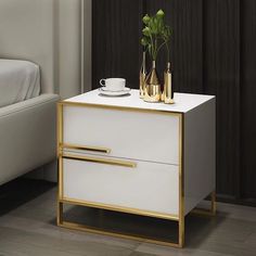 a white and gold side table with two vases on it next to a bed