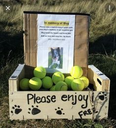 a crate filled with green tennis balls sitting on top of a grass covered field next to a sign that says please enjoy