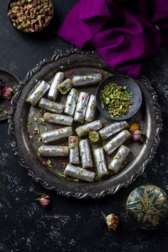 some food is on a metal plate and next to two bowls filled with nuts, pistachios and other foods