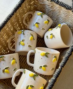 five white cups with lemons painted on them sitting in a wicker basket next to a table cloth