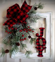 a red and black plaid christmas wreath hanging on a white door with the word joy