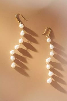 two pairs of earrings with pearls hanging from the end of each earring, on a beige background