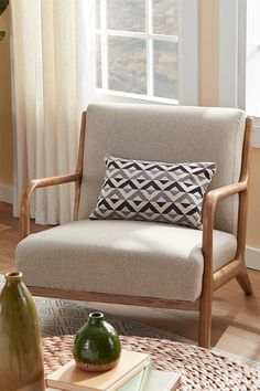 a chair with a pillow on it in front of a window and a vase next to it