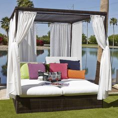 an outdoor daybed with pillows and curtains on the top, next to a lake