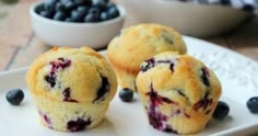 three blueberry muffins on a white plate with some berries in the background