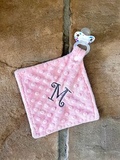 a pink bib with a monogrammed m on it and a pacifier hanging from the front