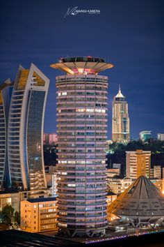 the tall building is lit up at night in front of other skyscrapers and buildings