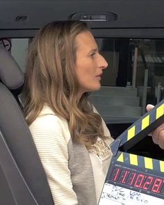 a woman sitting in the back seat of a car holding a movie clapper and talking to someone