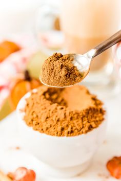 a spoon full of powdered brown food on top of a white bowl next to a glass of milk