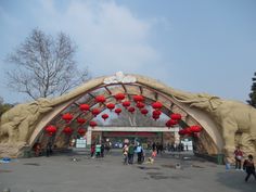 people are walking around in front of an arch with red lanterns hanging from the ceiling