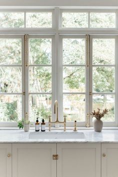 a white kitchen with marble counter tops and gold faucets on the windowsill