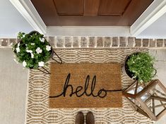 a welcome mat with the word hello written on it next to two potted plants