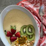 a white bowl filled with fruit and nuts next to a spoon on top of a red towel