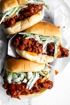 three sloppy joe sandwiches sitting on top of white paper