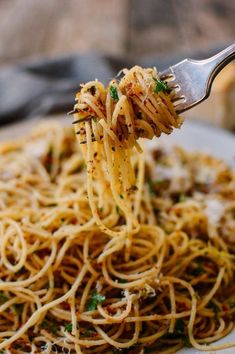 a fork full of spaghetti being lifted from a white plate with parmesan cheese